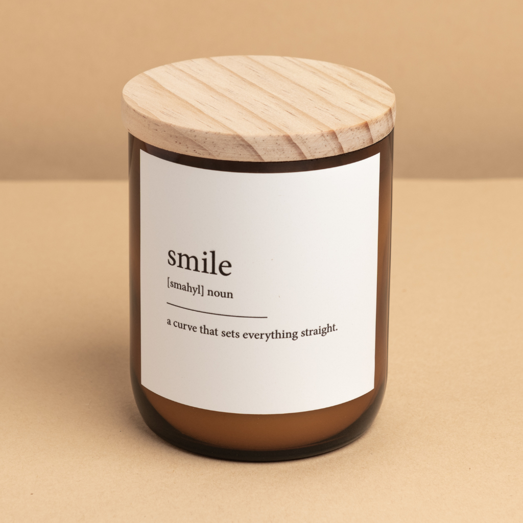 The Commonfolk scented candle, with a wooden lid and a label that defines 'smile' as a curve that sets everything straight, is set against a beige background.