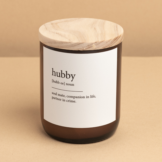 The Commonfolk scented candle with a wooden lid in an amber glass jar, labeled 'hubby' with a definition in brackets 'soul mate, companion in life, partner in crime.'.