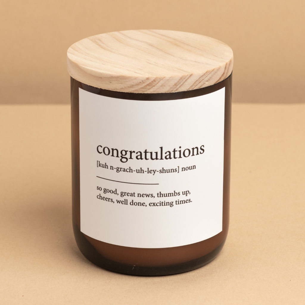 The Commonfolk scented medium-sized candle with a wooden lid and a label that reads 'congratulations', defined as 'good news, thumbs up, well done, exciting time'. The candle is set against a neutral background.