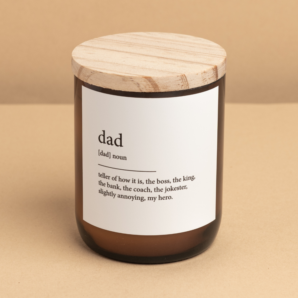 The Commonfolk scented candle is in an amber glass jar with a wooden lid, labeled 'dad,' which stands for 'dictionary meaning candle.'