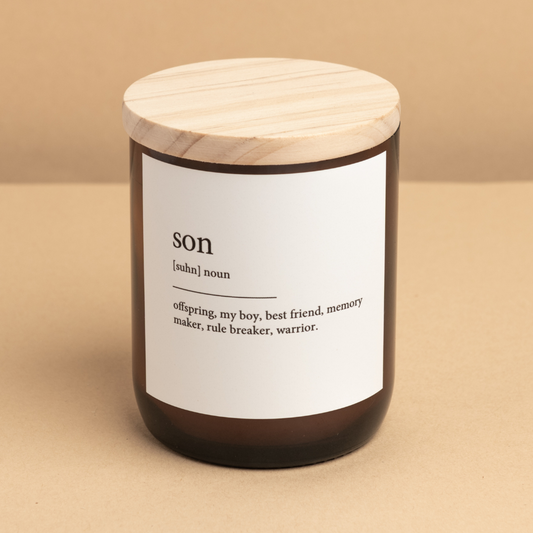 The Commonfolk scented candle has a white label that reads 'son' in brackets, followed by definitions. The candle has a wooden lid and is placed against a beige background.