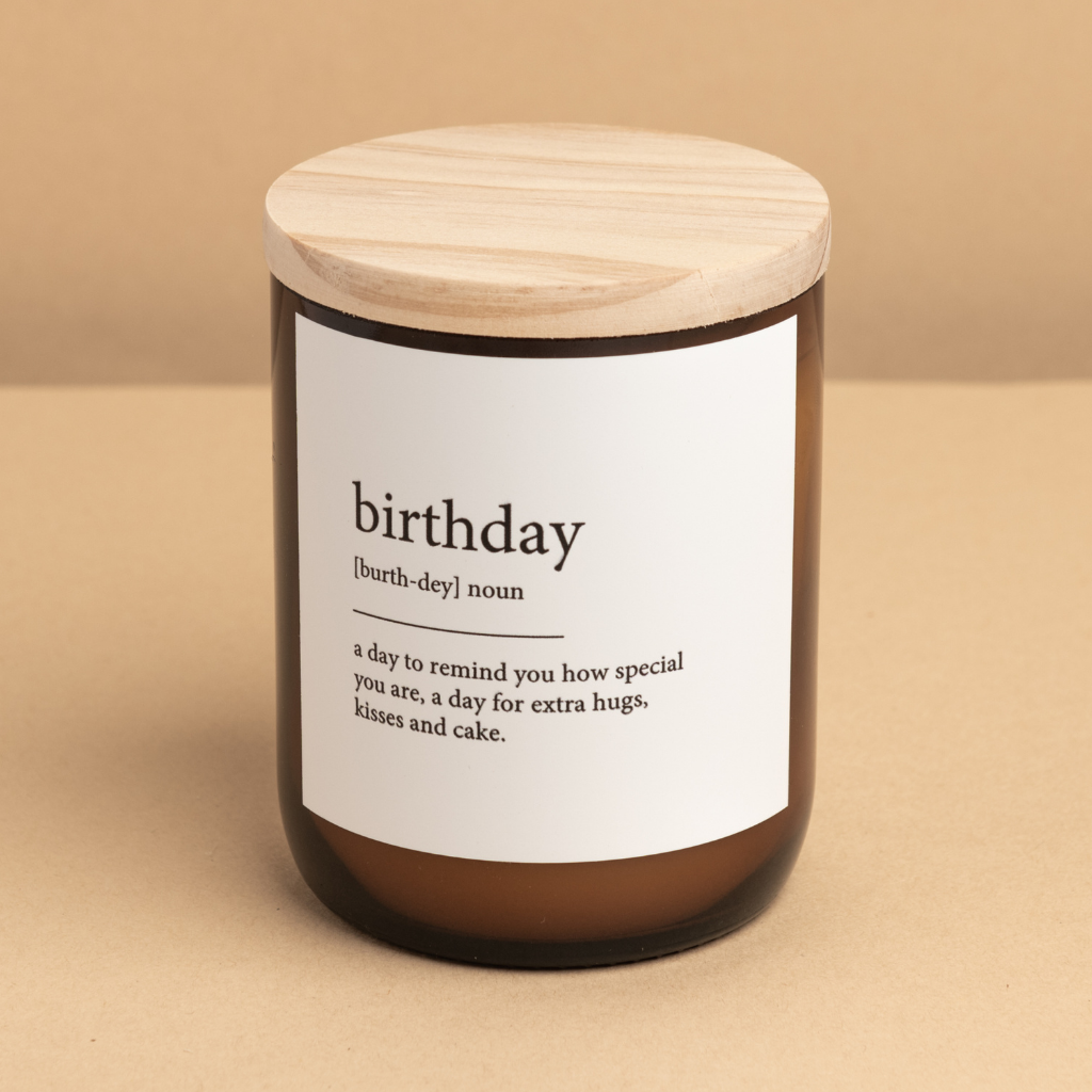 The Commonfolk scented candle with a wooden lid, labeled 'birthday,' is defined as 'a day to remind you how special you are, a day for extra hugs, kisses, and cake.'