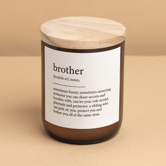 The Commonfolk scented candle with a beige label that defines 'brother' and a wooden lid, set against a beige background.