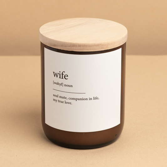 The Commonfolk scented candle has a white label that defines 'wife' in brackets as 'soul mate, companion in life, my true love.' The candle is in a brown jar with a wooden lid.