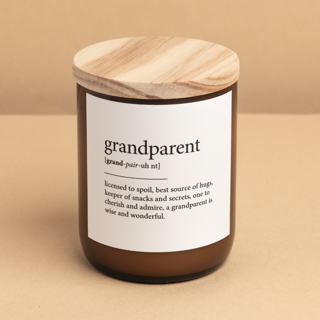 The Commonfolk scented candle, with a label that defines 'grandparent' and a wooden lid, is placed on a beige surface.