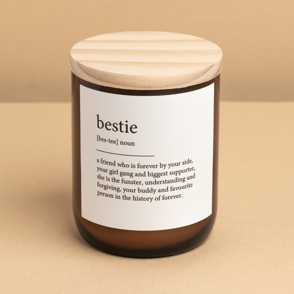 The Commonfolk scented medium-sized amber jar candle with a wooden lid, labeled 'bestie' which stands for 'buddy and favourite person in the history of forever'. The candle is made with soy and coconut wax and is unlit.