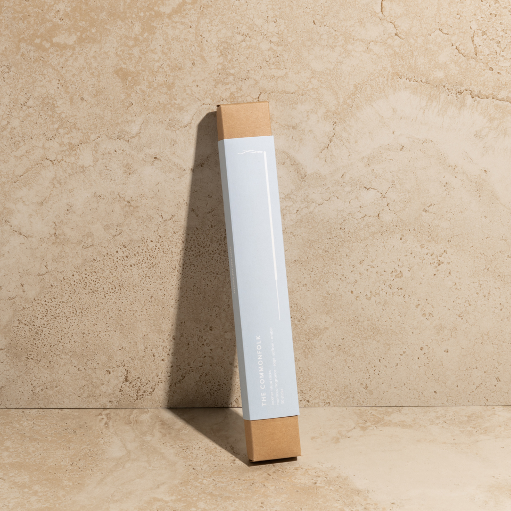The Commonfolk scented incense ritual sticks pack in light blue color is placed upright against a textured wall, with a shadow cast on the wall.