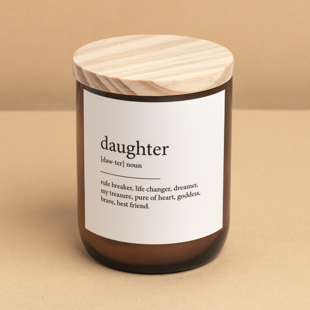 The Commonfolk scented candle comes in a clear amber jar with a wooden lid, labeled 'daughter' with dictionary definition text.