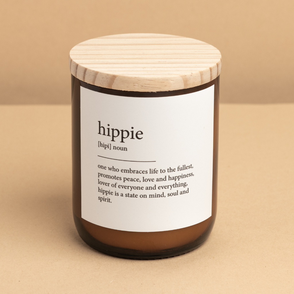 The Commonfolk scented candle with a wooden lid in an amber jar with a white label that defines 'hippie'.