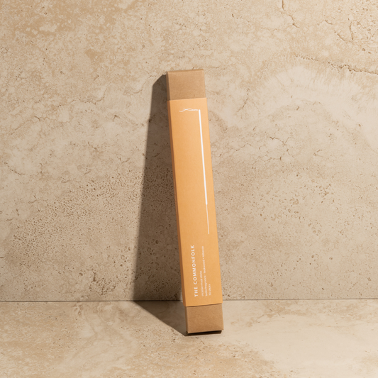 The Commonfolk scented incense ritual sticks pack in orange color is placed upright against a textured wall, with a shadow cast on the surface.