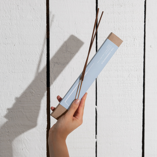 A person holds a pack of incense ritual sticks in front of a plain white wall.