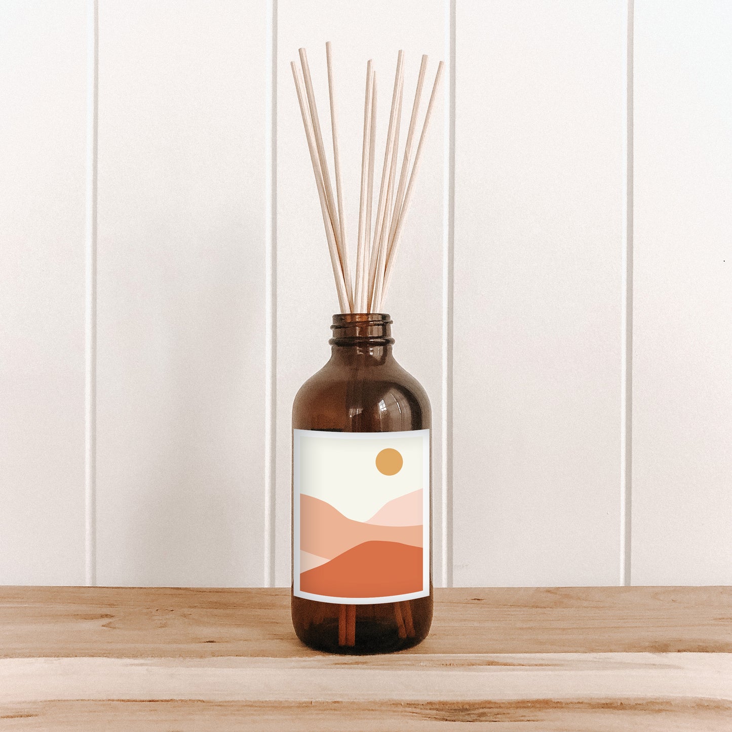 The Commonfolk room diffuser with natural bamboo reed sticks in an amber glass bottle with a label featuring a sun and desert landscape.