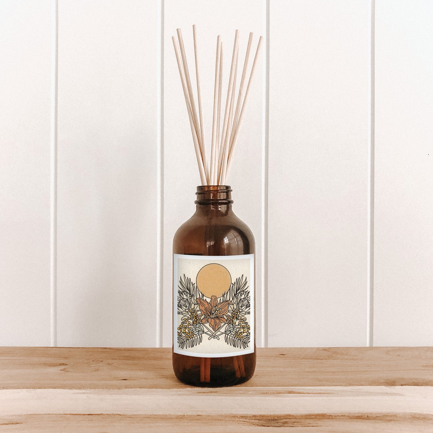 The Commonfolk room diffuser with natural bamboo reed sticks in an amber glass bottle features a label with floral artwork.