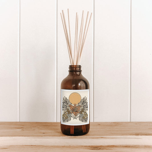 The Commonfolk room diffuser with natural bamboo reed sticks in an amber glass bottle features a label with floral artwork.
