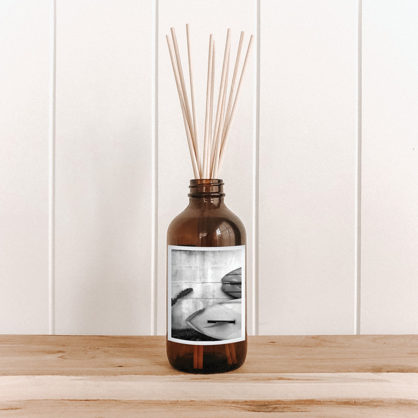 The Commonfolk room diffuser with natural bamboo reed sticks in a clear glass bottle features a black and white photo of a surfboard on the label.