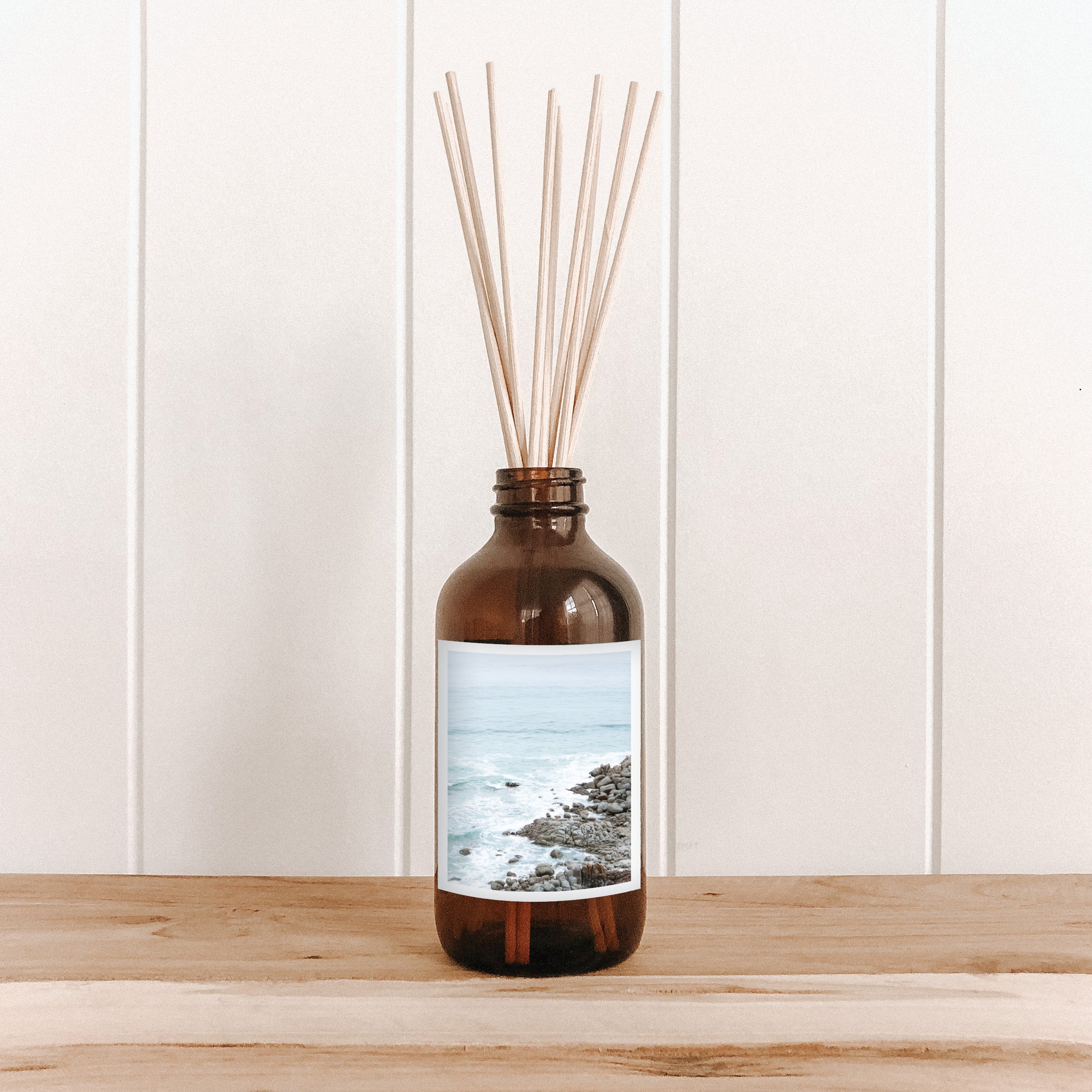 The Commonfolk room diffuser with natural bamboo reed sticks in a brown bottle features a label with a photo of a sea stack.