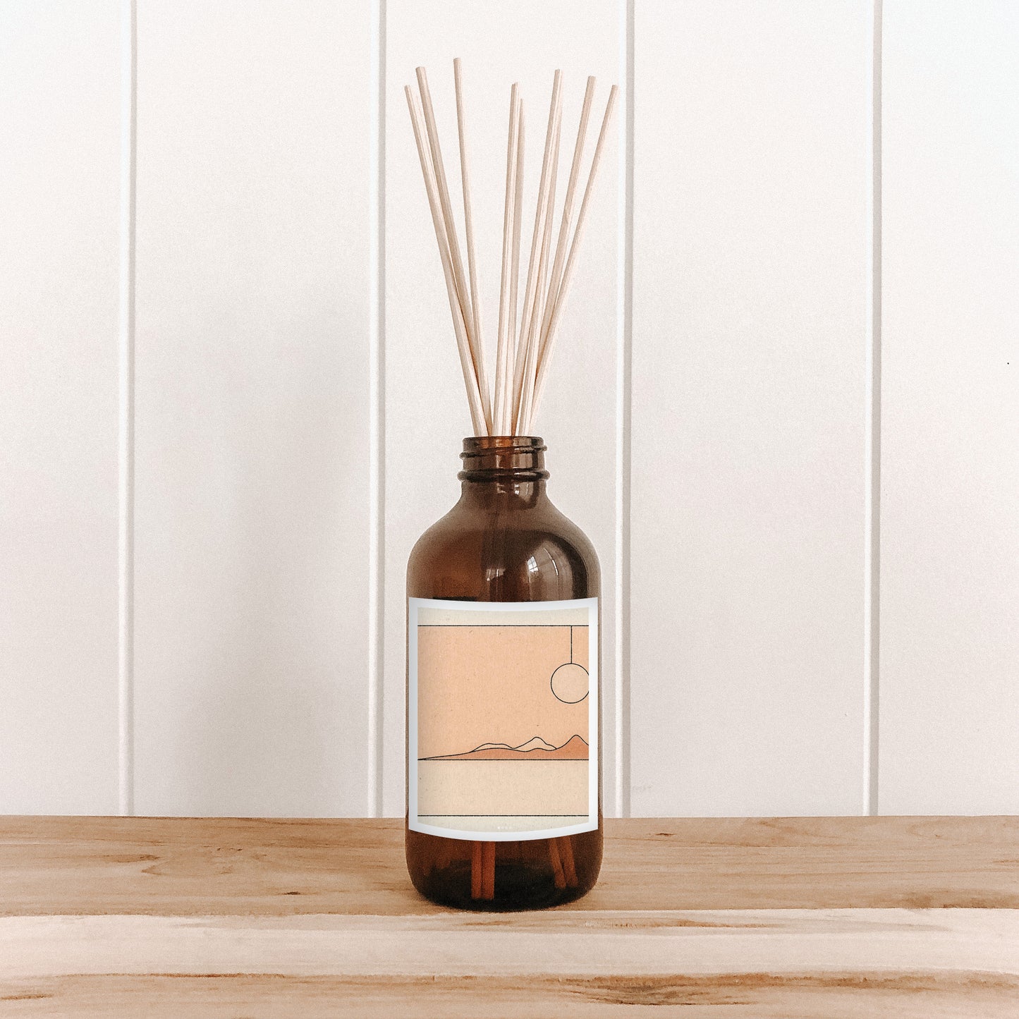 The Commonfolk room diffuser with natural bamboo reed sticks in a clear glass bottle features a label with artwork.