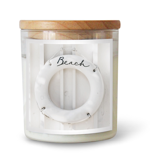 The Commonfolk scented white candle, with a label featuring the word 'Beach' and a circular design, is topped with a natural wood lid.