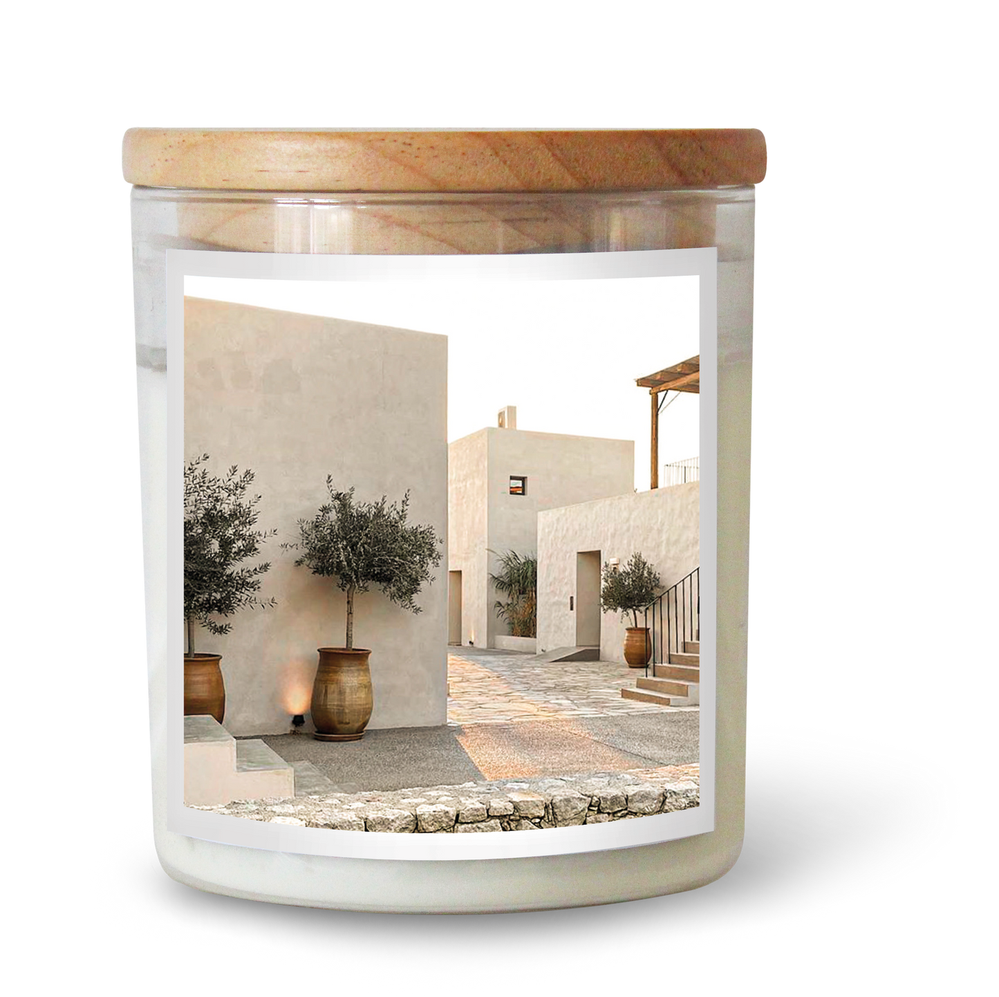 The Commonfolk scented candle features white wax, a clear glass jar, and a wooden lid, with an image of a serene street scene that includes buildings and a tree.