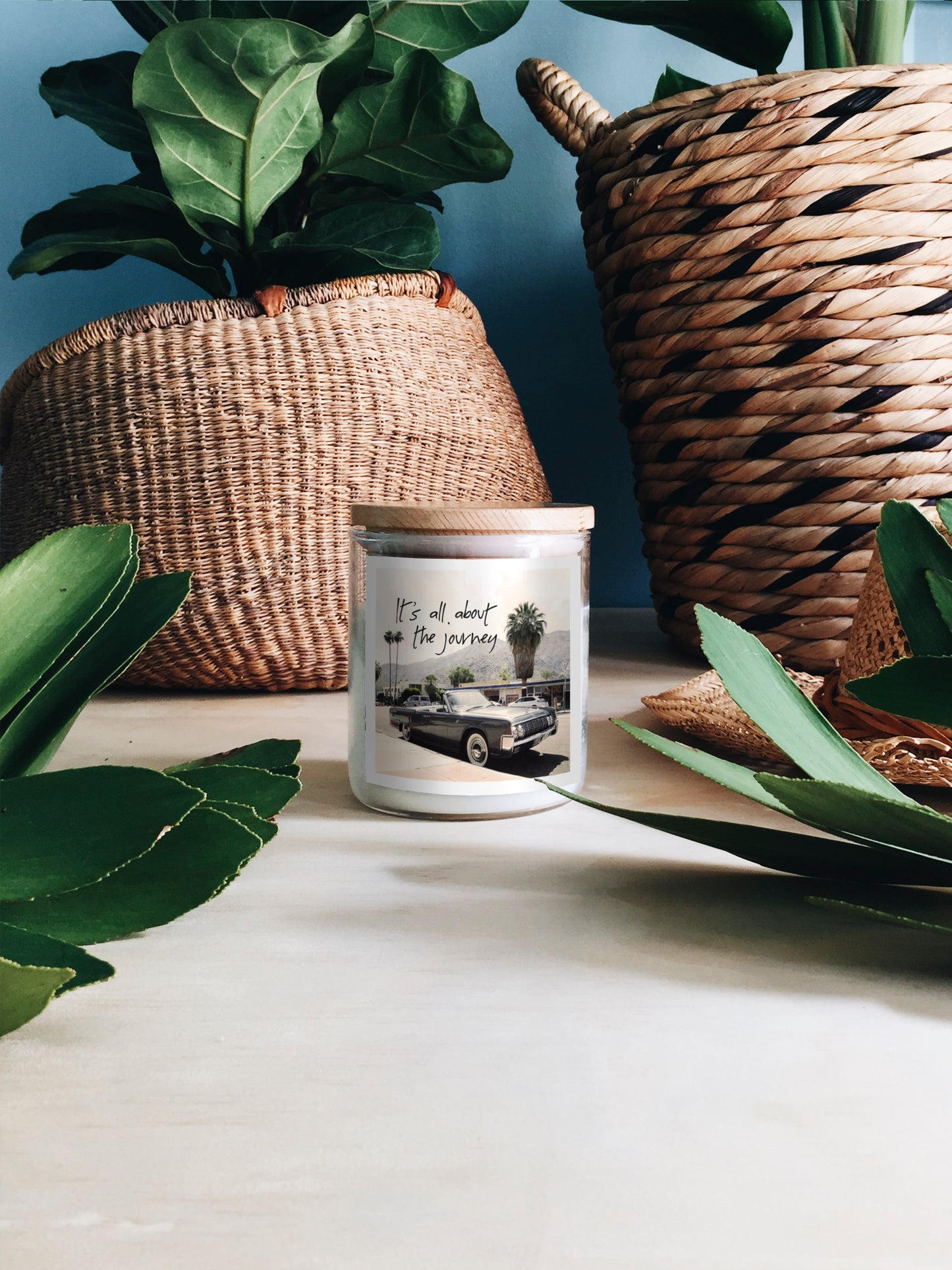 A candle placed beside a basket filled with various green plants, creating a cozy and natural ambiance.
