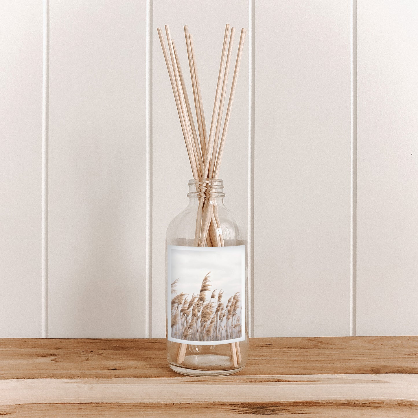 The Commonfolk room diffuser with natural bamboo reed sticks in a clear glass bottle features a label with pampas grass imagery.