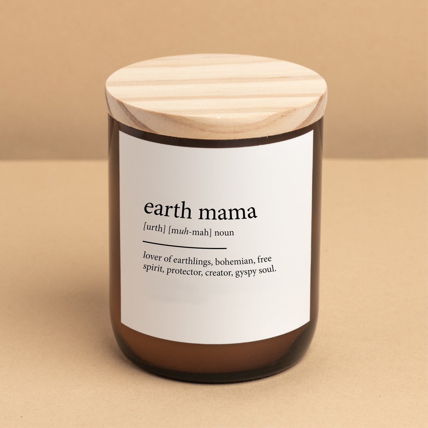 The Commonfolk scented candle comes in a clear amber jar with a wooden lid, labeled 'earth mama' with a definition in brackets: 'lover of earthlings, bohemian, free spirit, protector, creator, gypsy soul.'