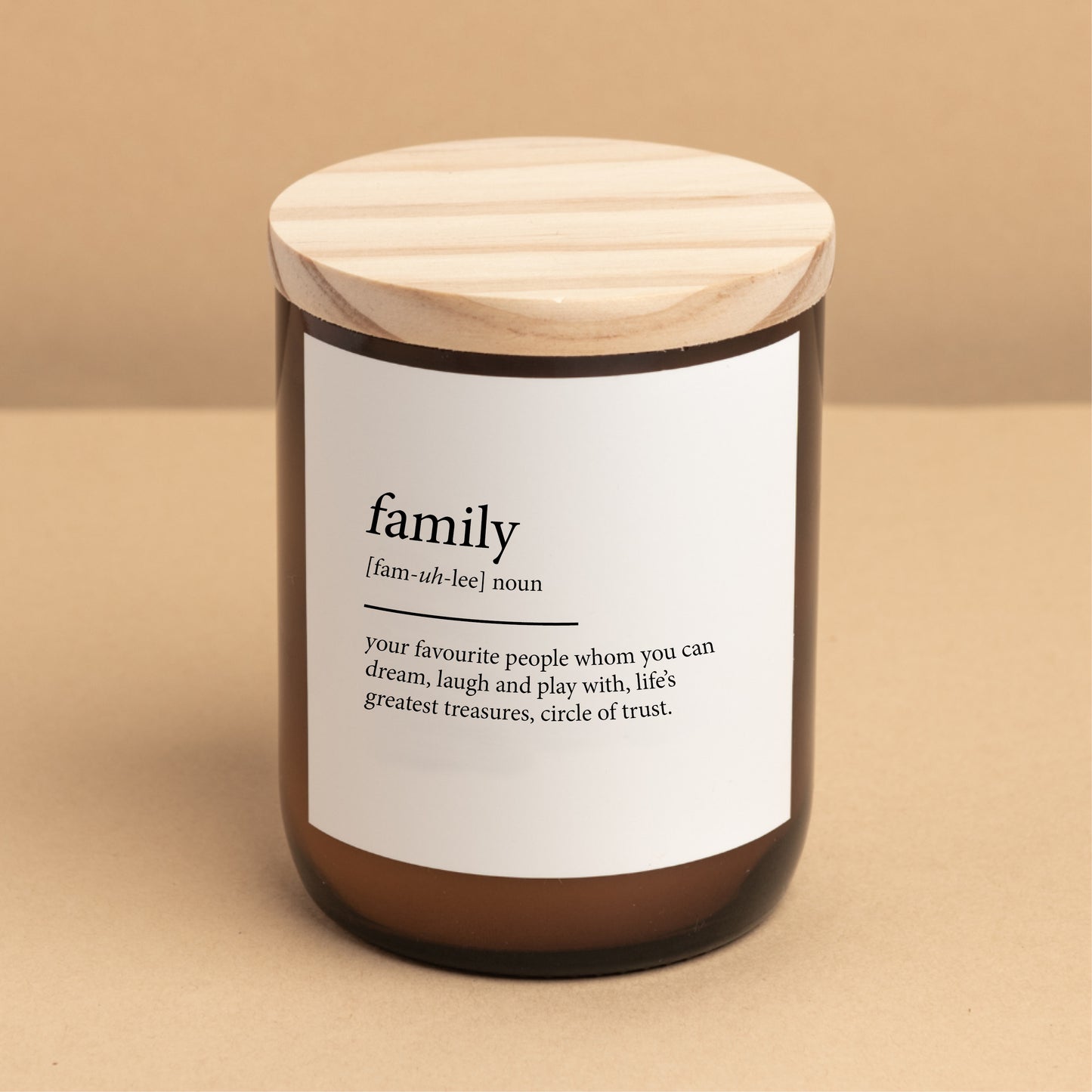 The Commonfolk scented candle comes in a glass jar with a wooden lid, labeled 'family,' with a definition below the word 'family' written in a quote style.