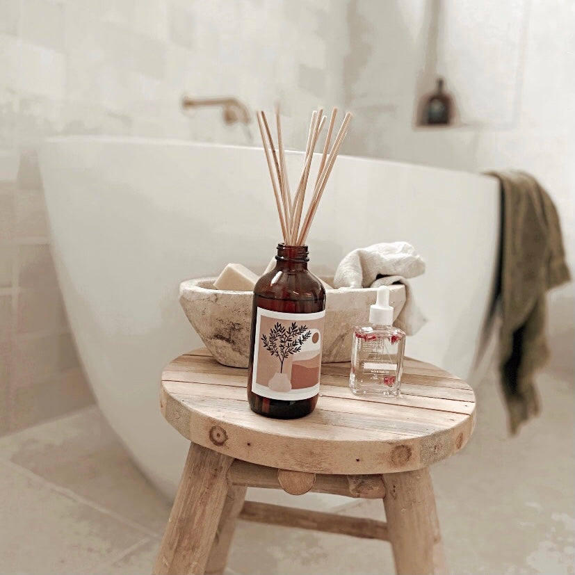 A wooden stool holding a bottle of room diffuser and a neatly folded towel.