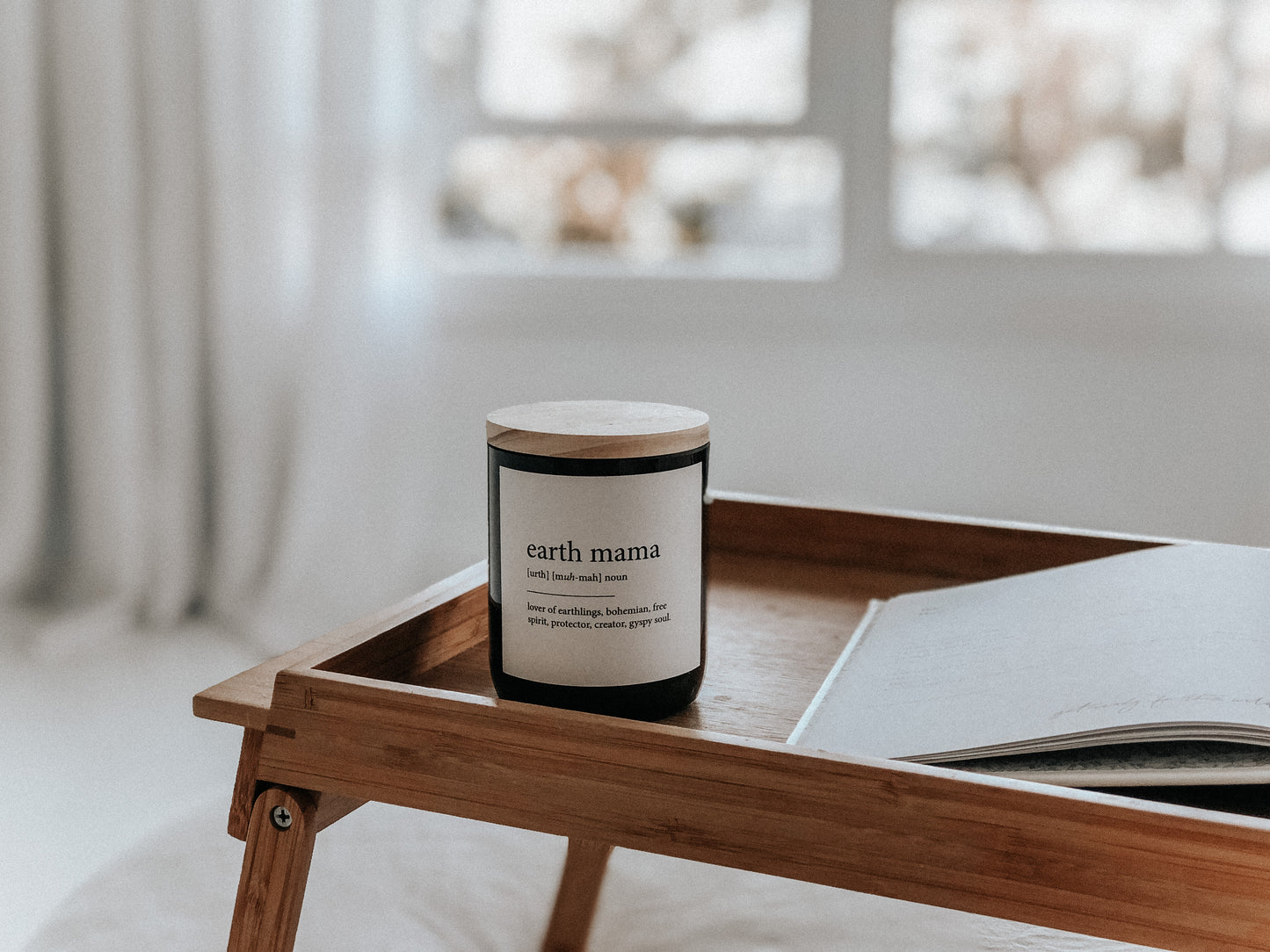A wooden tray holds a Commonfolk scented candle and an open book, creating a cozy and inviting atmosphere.