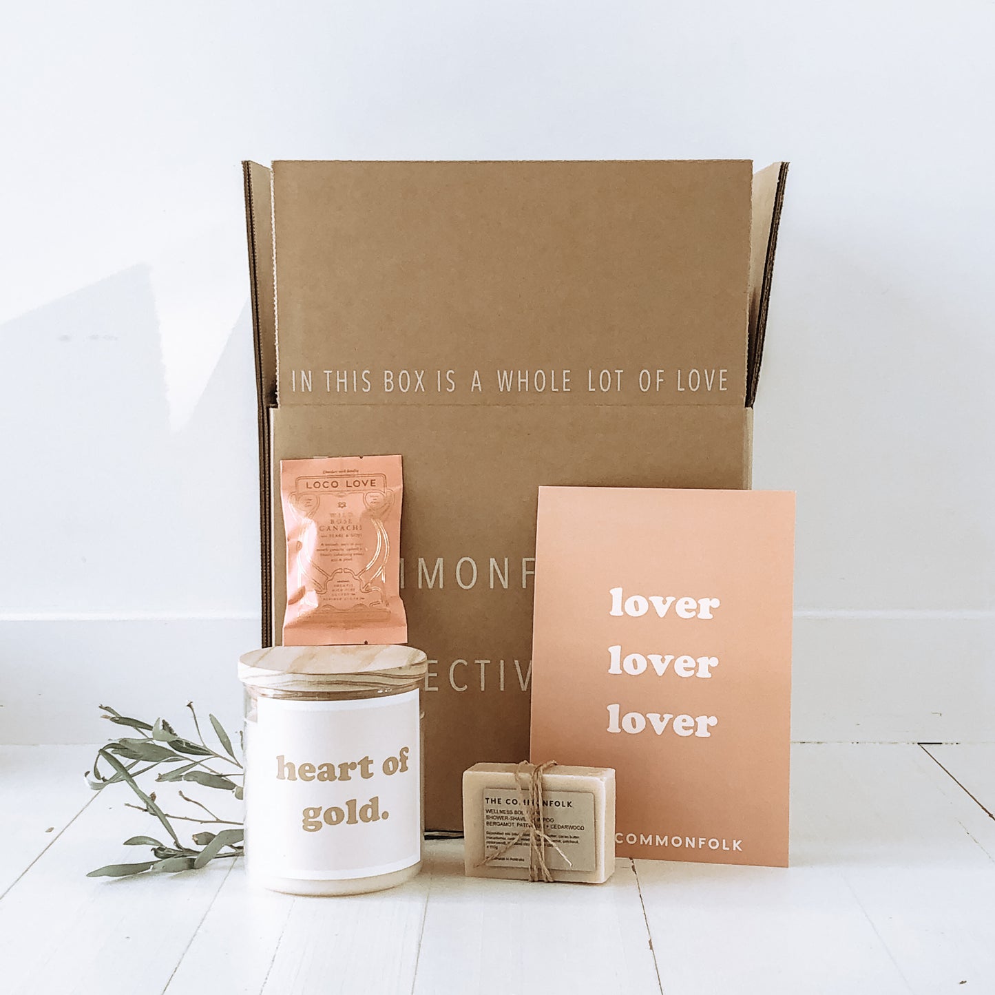 The Commonfolk gift includes a candle, a packet of body bar soap, chocolate, and a gift card with a personal message. The items are displayed on a white background.