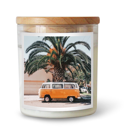 The Commonfolk scented clear jar candle has a wooden lid with a label featuring a vintage photo of a van and palm trees.
