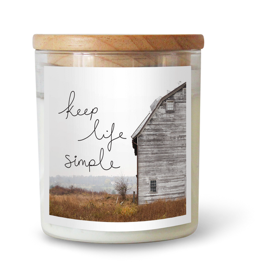 The Commonfolk scented white candle with a wooden lid features a label with the text 'Keep Life Simple' and an image of a rustic wooden shed.