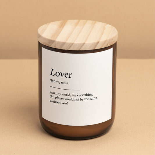 The Commonfolk scented candle has a label that reads 'Lover,' defined as 'you, my world, my everything. The planet would not be the same without you!' The candle is in an amber jar with a wooden lid.