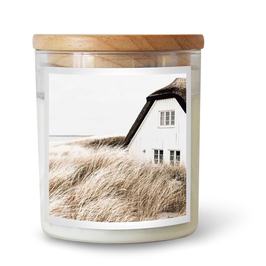 The Commonfolk scented candle has a label featuring a white house by the sea, with tall grass in the foreground.