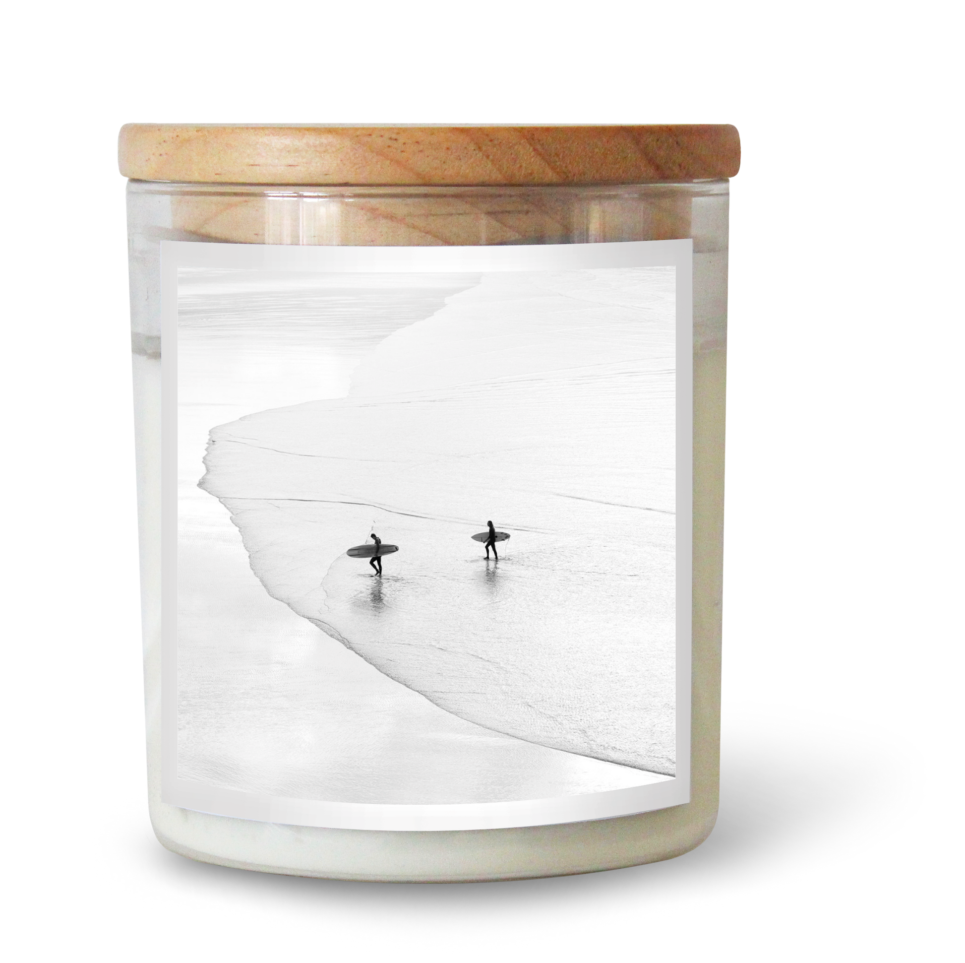 The Commonfolk scented candle has white wax, housed in a clear glass jar with a wooden lid. The wick appears to be in a surf shape, and there are decorative surfboard-like figures beside the jar.