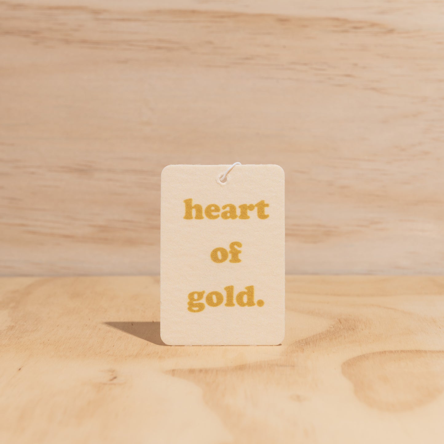 The Commonfolk air freshener, with the text 'heart of gold' printed in the center, is displayed against a wooden background.
