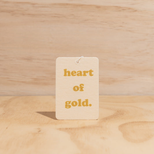 The Commonfolk air freshener, with the text 'heart of gold' printed in the center, is displayed against a wooden background.