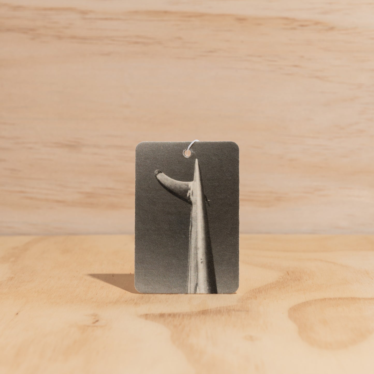 The Commonfolk air freshener is displayed on a wooden surface, with a fin print on the label.