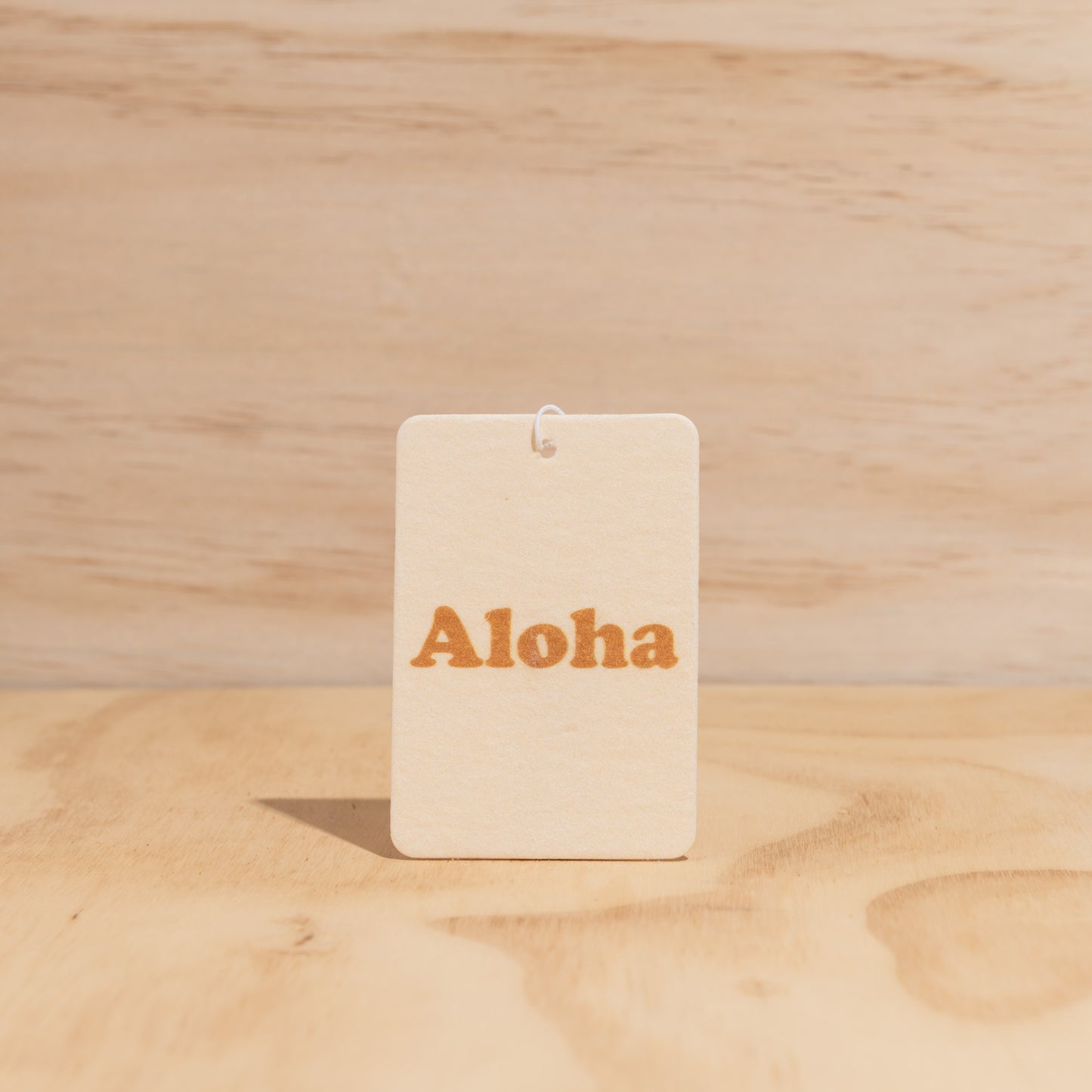 The Commonfolk air freshener with the word 'Aloha' printed in orange displays against a wooden background.