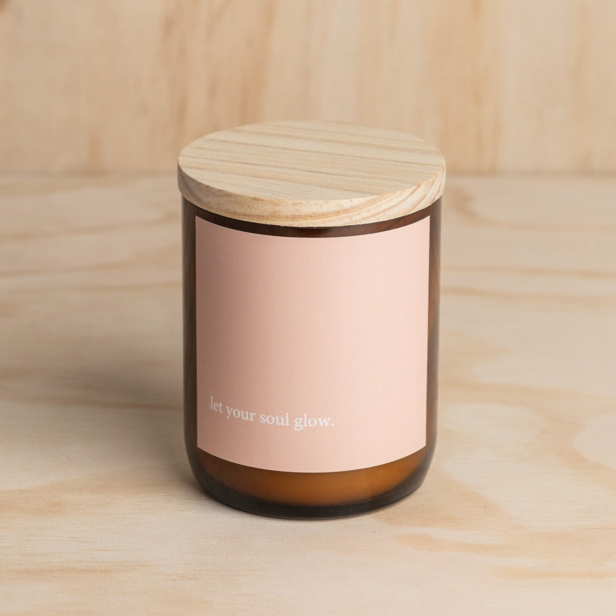 The Commonfolk scented mid-sized amber jar candle with a wooden lid, and a label that reads 'let your soul glow.'
