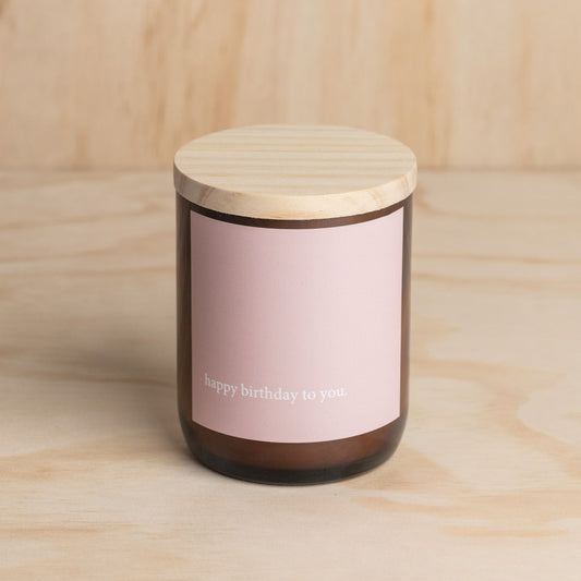 The Commonfolk scented candle with a wooden lid, labeled 'Happy Birthday to you' on a brown jar.