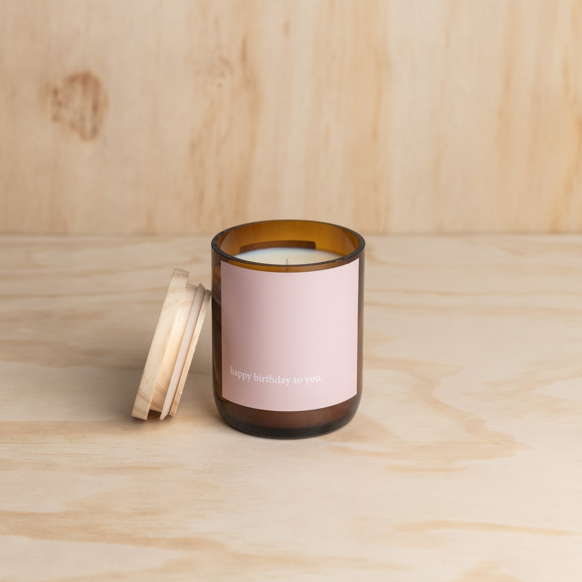 A pink candle placed on a rustic wooden table, creating a warm and inviting atmosphere.