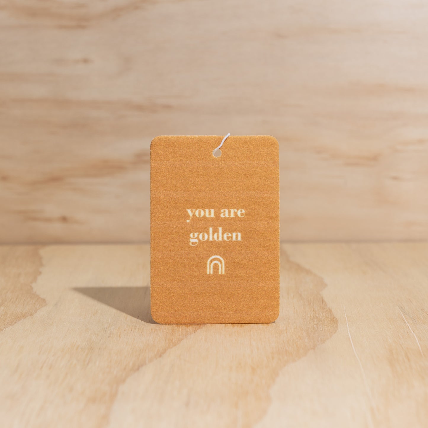 The Commonfolk air freshener with the text 'you are golden' printed on it, is displayed against a wooden background.