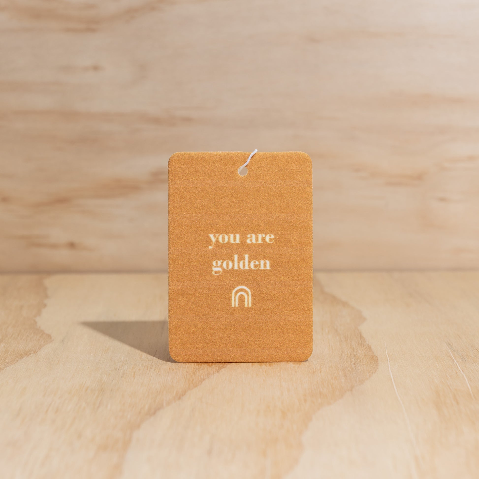 The Commonfolk air freshener with the text 'you are golden' printed on it, is displayed against a wooden background.