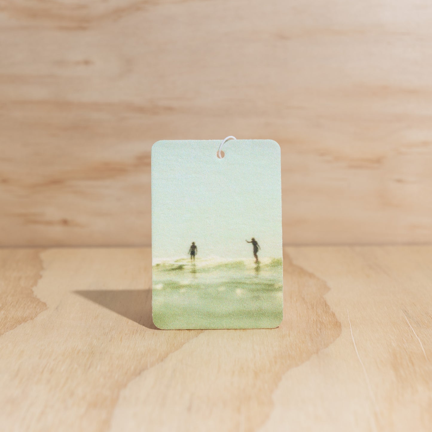 The Commonfolk air freshener, with a depiction of a beach scene, is displayed against a wooden background.