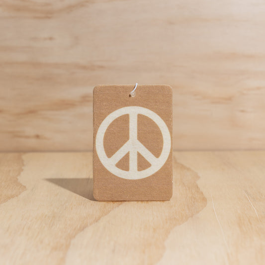 The Commonfolk air freshener with a white peace sign symbol displays on a wooden surface.