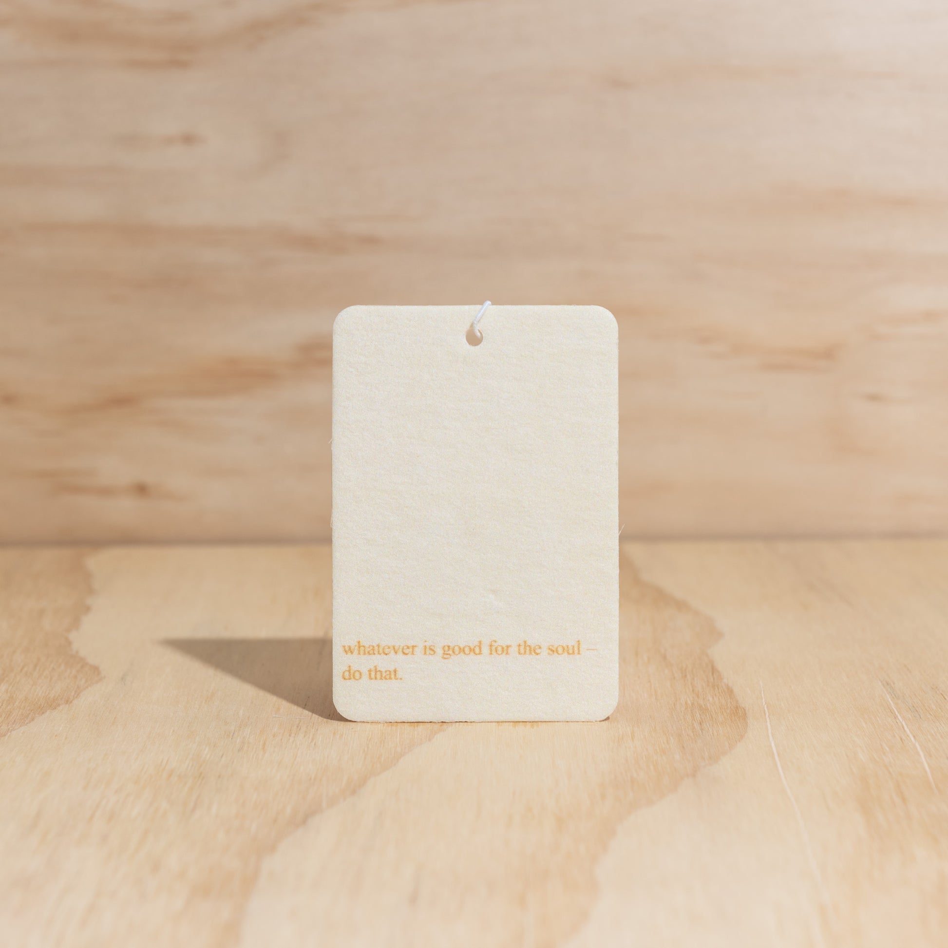 The Commonfolk air freshener card with the text 'whatever is good for the soul - do that' printed on it, displayed against a wooden background.