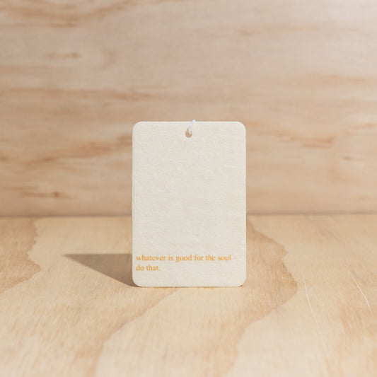 The Commonfolk air freshener card with the text 'whatever is good for the soul - do that' printed on it, displayed against a wooden background.