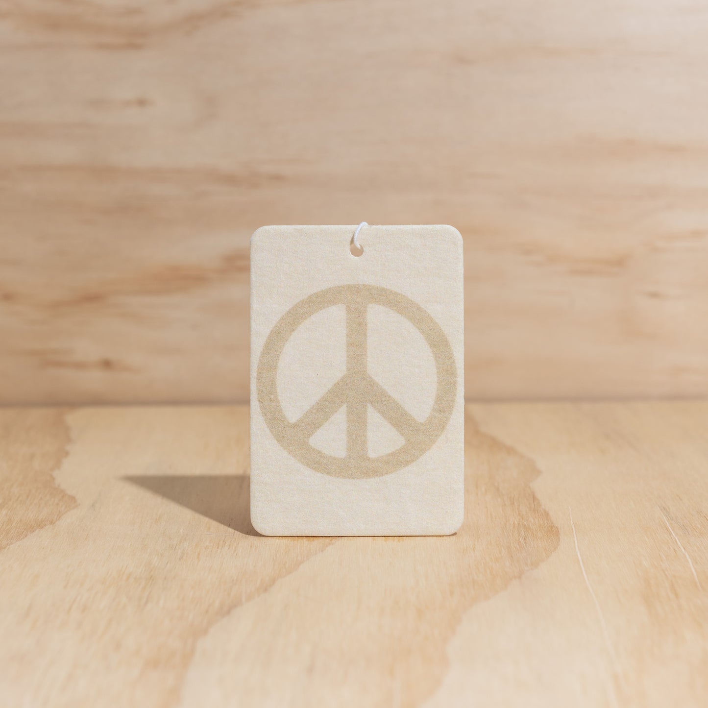 The Commonfolk air freshener with a peace sign in the center displays on a wooden surface.