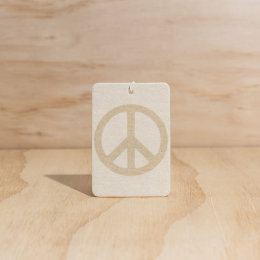 The Commonfolk air freshener with a peace sign in the center displays on a wooden surface.